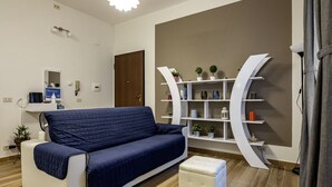 A modern living room with a sofa, ottoman, white curved bookshelf, and a small table with a plant. - GuestHost - La Spezia Mon Amour - Pet Friendly (La Spezia)