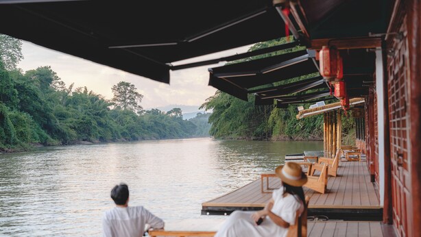 A wooden deck with benches overlooking a river, surrounded by lush greenery. - Long Chuan River Kwai (Thong Pha Phum)