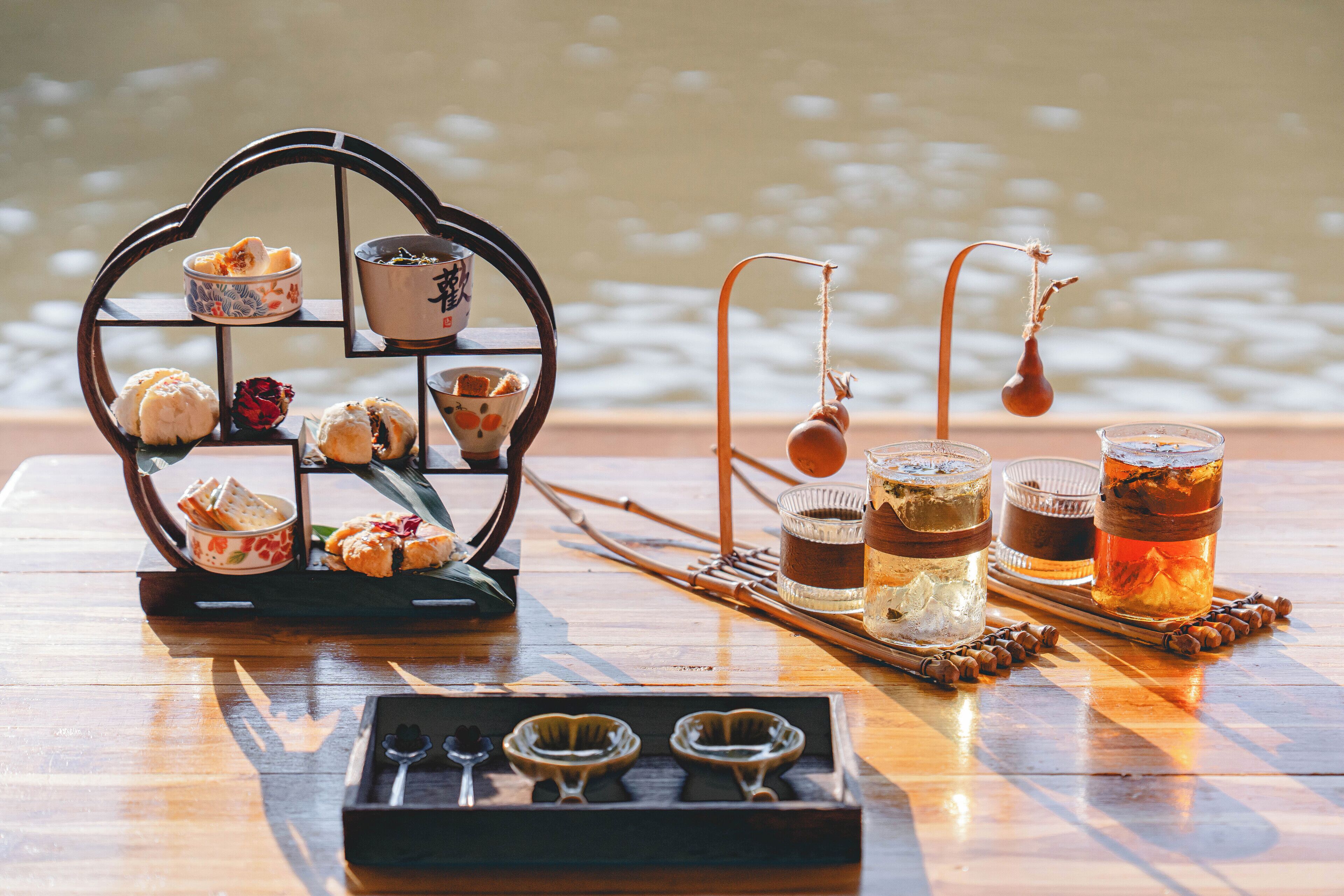 A wooden table with a tea set, including teapots, cups, and a tray with pastries.