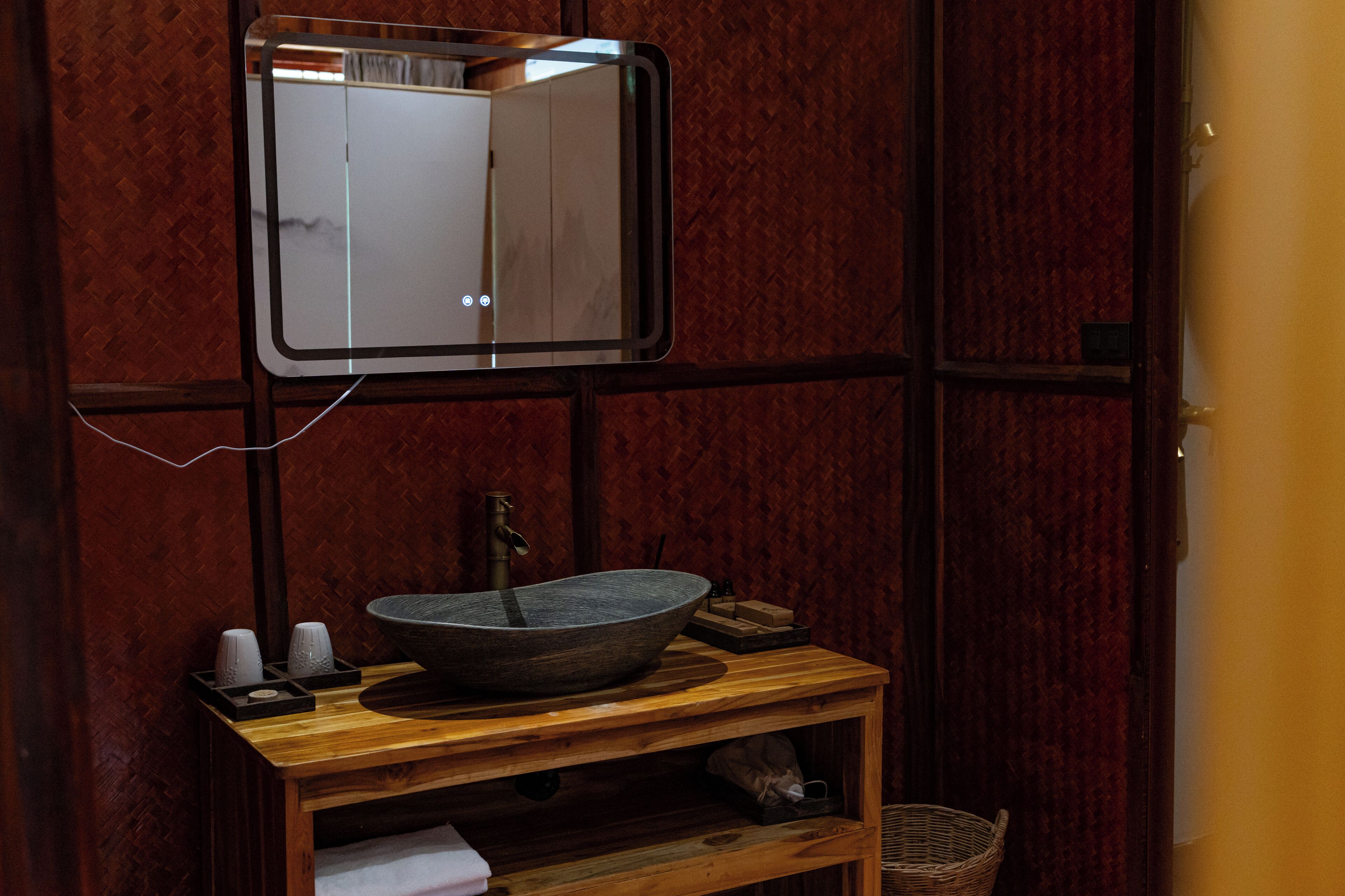 Un baño con tocador de madera, lavamanos tipo recipiente, espejo y perchero para toallas.