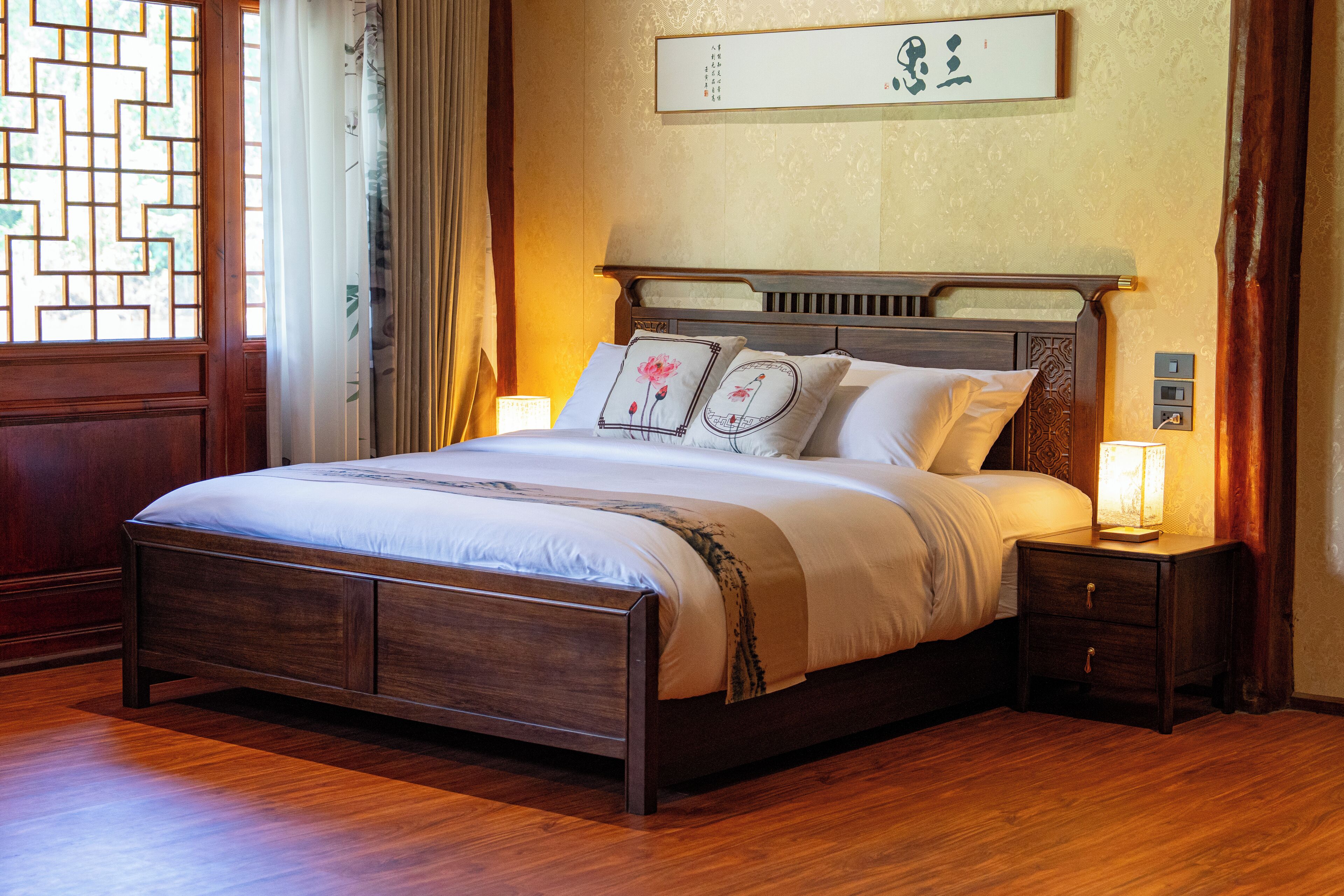 A neatly made bed with a wooden frame, a bedside table with a lamp, and a wall-mounted artwork.