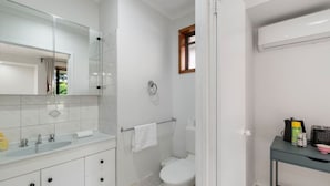 A modern bathroom with a large mirror, a sink with two faucets, a toilet, and a shower area. - Budget 1-Bed Studio Near Top Malls & Transit! (Robertson)
