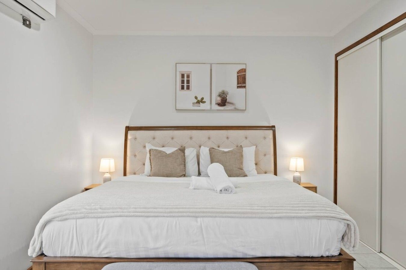 A neatly made bed with a tufted headboard, two bedside lamps, and a framed picture above the bed.