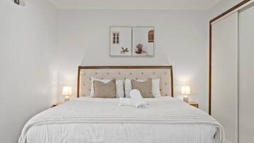 A neatly made bed with a tufted headboard, two bedside lamps, and a framed picture above the bed.