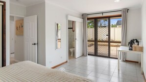 A bedroom with a bed, a desk, a chair, a toilet, and a sliding glass door leading to an outdoor area. - Affordable 1-Bed Studio Close to Malls & Transit! (Robertson)
