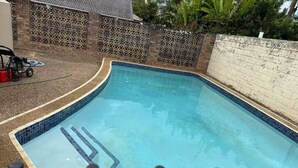 A rectangular swimming pool with a tiled edge and a ladder leading into the water. - Affordable 1-Bed Studio Close to Malls & Transit! (Robertson)