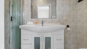 A bathroom with a glass shower enclosure, a white sink with a mirror above, and a toilet to the right. - Affordable 1-Bed Studio Close to Malls & Transit! (Robertson)
