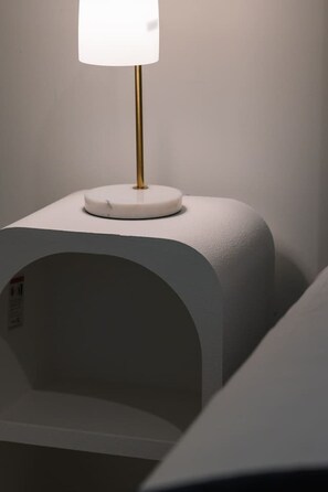 A white bedside table with a lamp and a white, curved bedside shelf. - Affordable 1-Bed Studio Close to Malls & Transit! (Robertson)