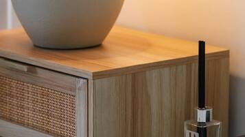 A bedside table with a lamp, a remote control, and a bottle of perfume.