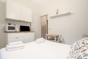 Un dormitorio con cama, escritorio, silla, microondas y armario.