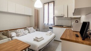 Una habitación de hotel compacta con cama, una kitchenette pequeña, una mesa de madera y un televisor.