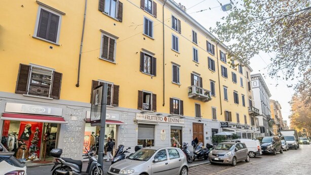 Una calle con coches aparcados y un edificio con varias ventanas y balcones.