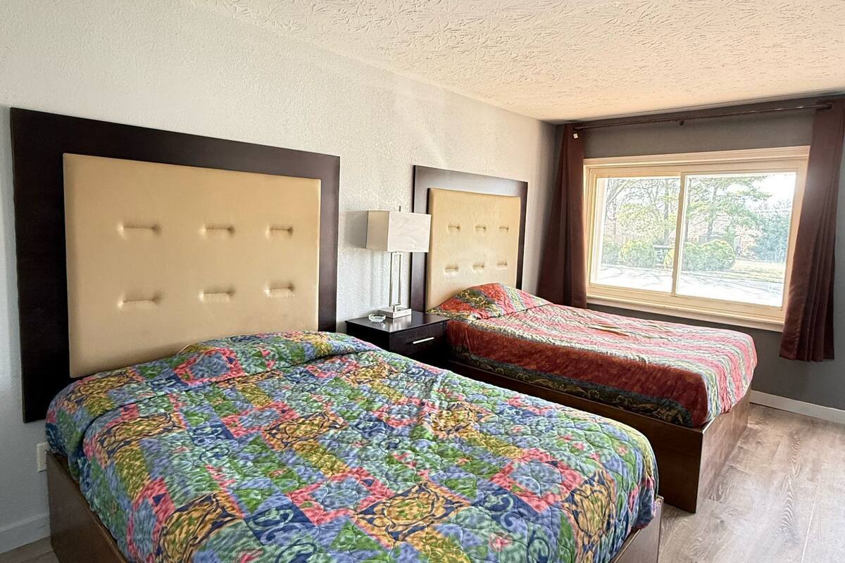 A hotel room with two beds, a large window with curtains, and a textured ceiling.