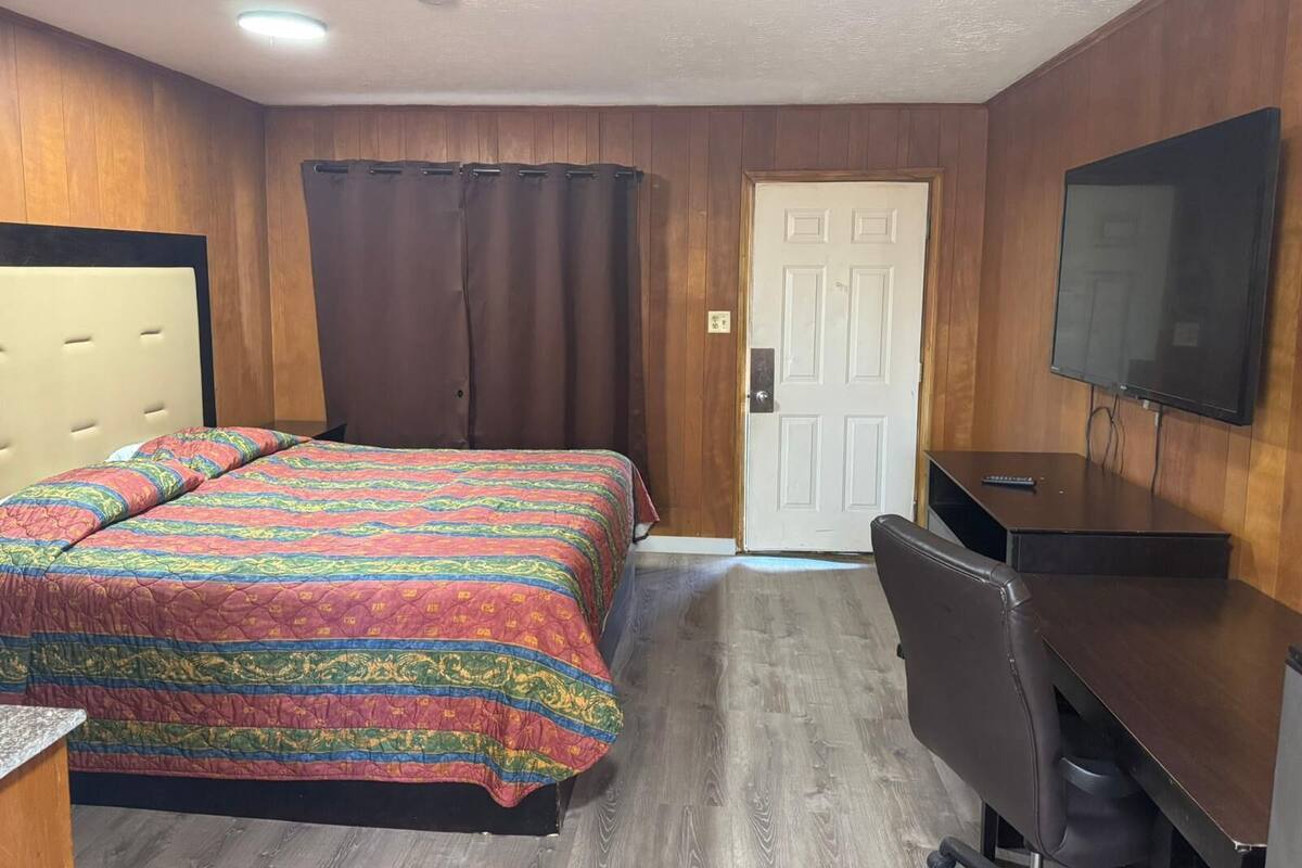 A bedroom with a bed, a desk, a chair, a television, and a door.