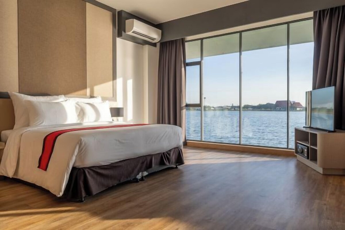 A modern hotel room with a large bed, a TV, and a view of a body of water.