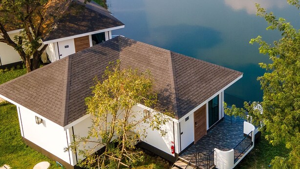 Una casa moderna con techo inclinado, un porche cubierto y vistas a un lago tranquilo.