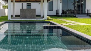Una casa moderna con piscina, un patio cubierto y un césped bien cuidado.
