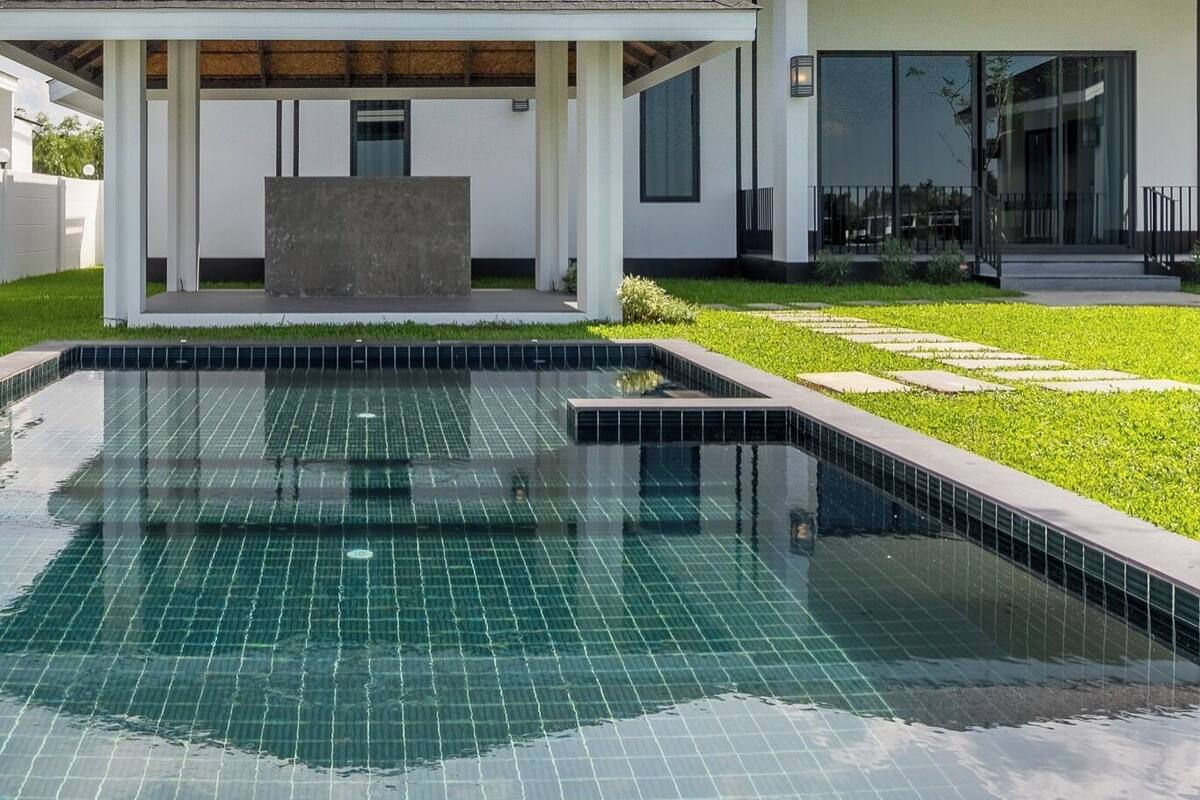 Una casa moderna con piscina, un patio cubierto y un césped bien cuidado.
