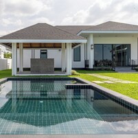 Una casa moderna con piscina, un patio cubierto y un césped bien cuidado.