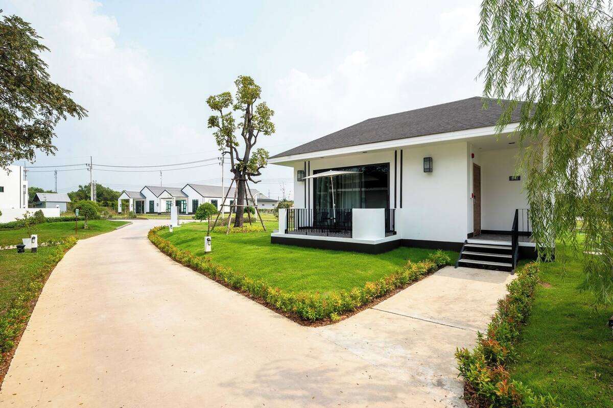 Una casa moderna con entrada pavimentada, césped cuidado y un gran árbol.