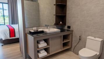A modern bathroom with a large mirror, a sink, and a toilet. There is a bed visible in the adjacent room.