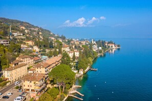 An aerial view of a coastal town with buildings along the waterfront, a clear sky, and a calm sea. - Roby Loft-direct Lake Access/beach (Gardone Riviera)