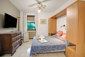 A bedroom with a bed, a dresser, a television, a ceiling fan, and a window with curtains. - Roby Loft-direct Lake Access/beach (Gardone Riviera)