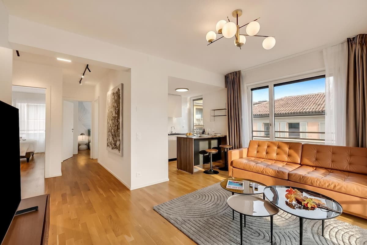A modern living room with a sofa, coffee table, and a dining area with a kitchen in the background.