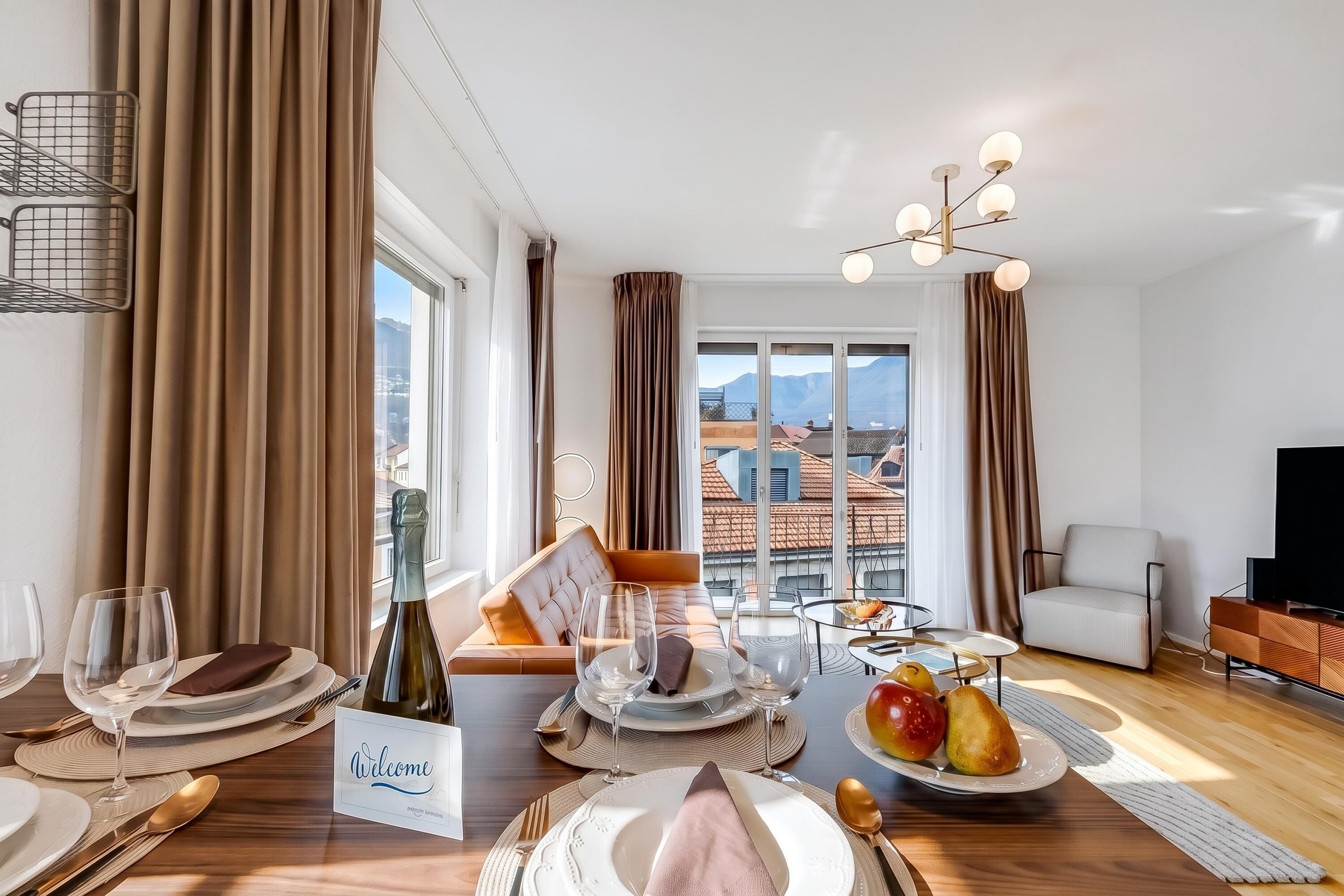 Una habitación bien iluminada con una mesa de comedor lista para una comida, un sofá y un televisor.