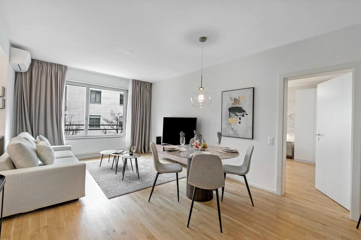 A modern living room with a sofa, dining table, chairs, and a TV.