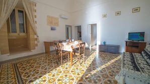 Zona pranzo con tavolo apparecchiato per quattro persone, divano e televisione su un mobile in legno.