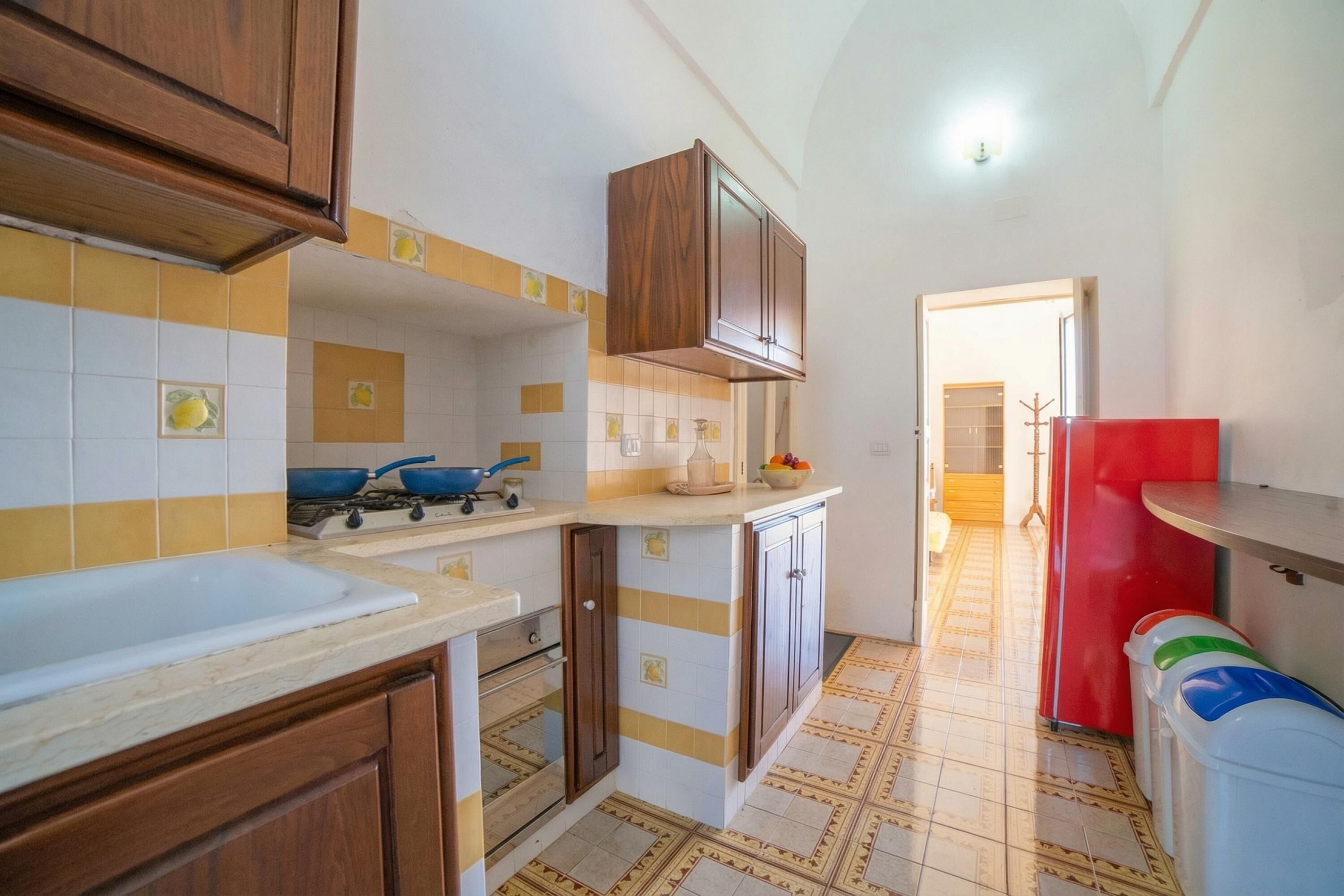A kitchen with wooden cabinets, a stove, a sink, and a red refrigerator.