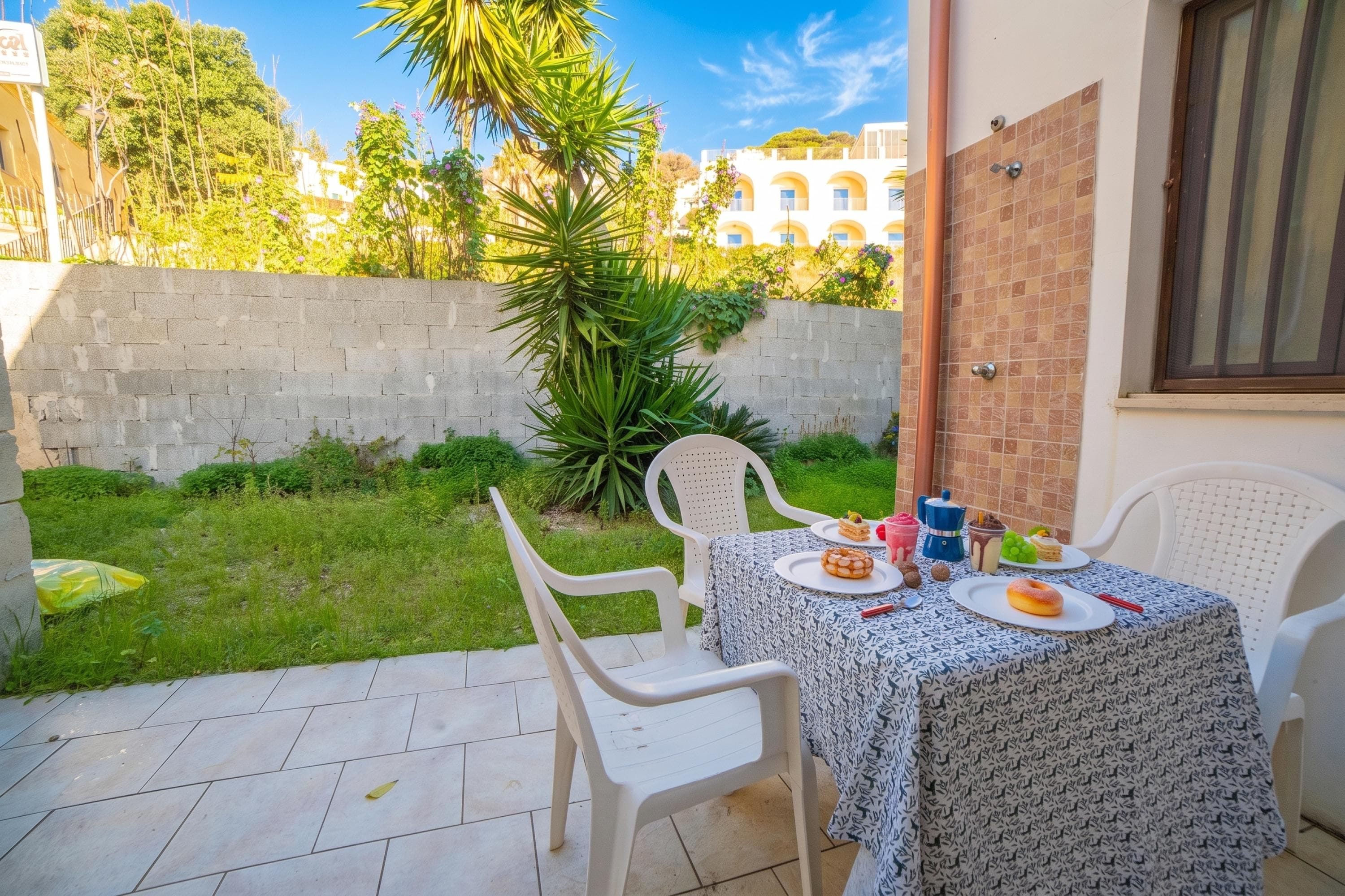 An outdoor patio with two white plastic chairs and a table set with plates of food, a coffee pot, and a teapot.
