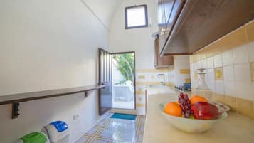 Una cocina con salpicadero de azulejos, un frutero sobre la encimera y una ventana con vistas al exterior.