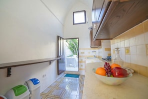 Una cocina estrecha con salpicadero de azulejos, un cuenco de fruta sobre la encimera y vistas al exterior.