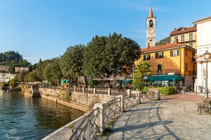 A riverside walkway with a stone railing, a clock tower, and buildings with balconies. - Casa Virginia (Laveno Mombello)