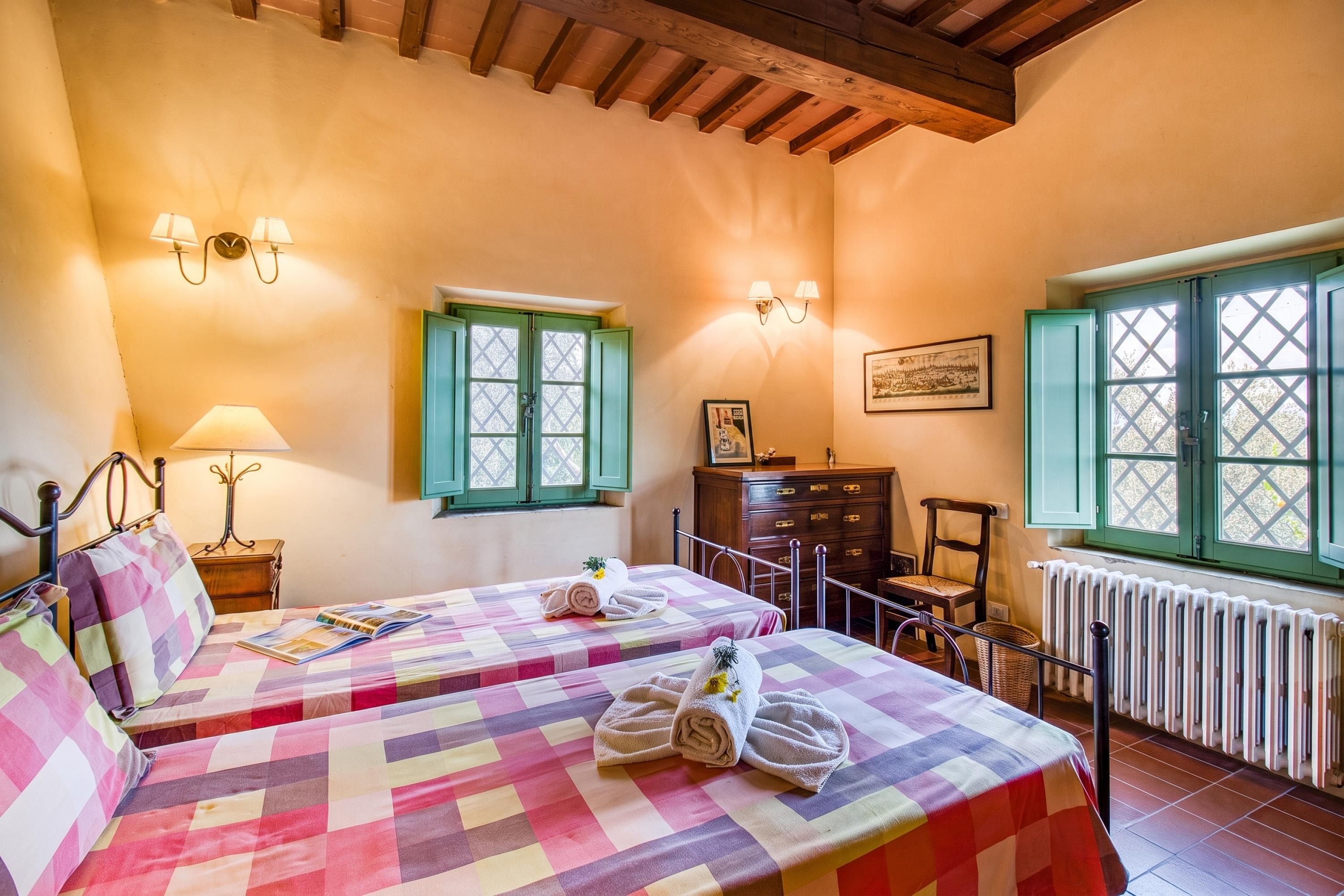 Habitación de hotel con dos camas, un aparador, una silla, una ventana con contraventanas y un radiador.