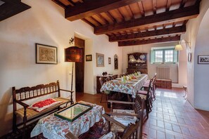Un coin repas avec une longue table, des chaises en bois et un banc. Les murs sont ornés de tableaux encadrés et un radiateur se trouve près de la fenêtre.