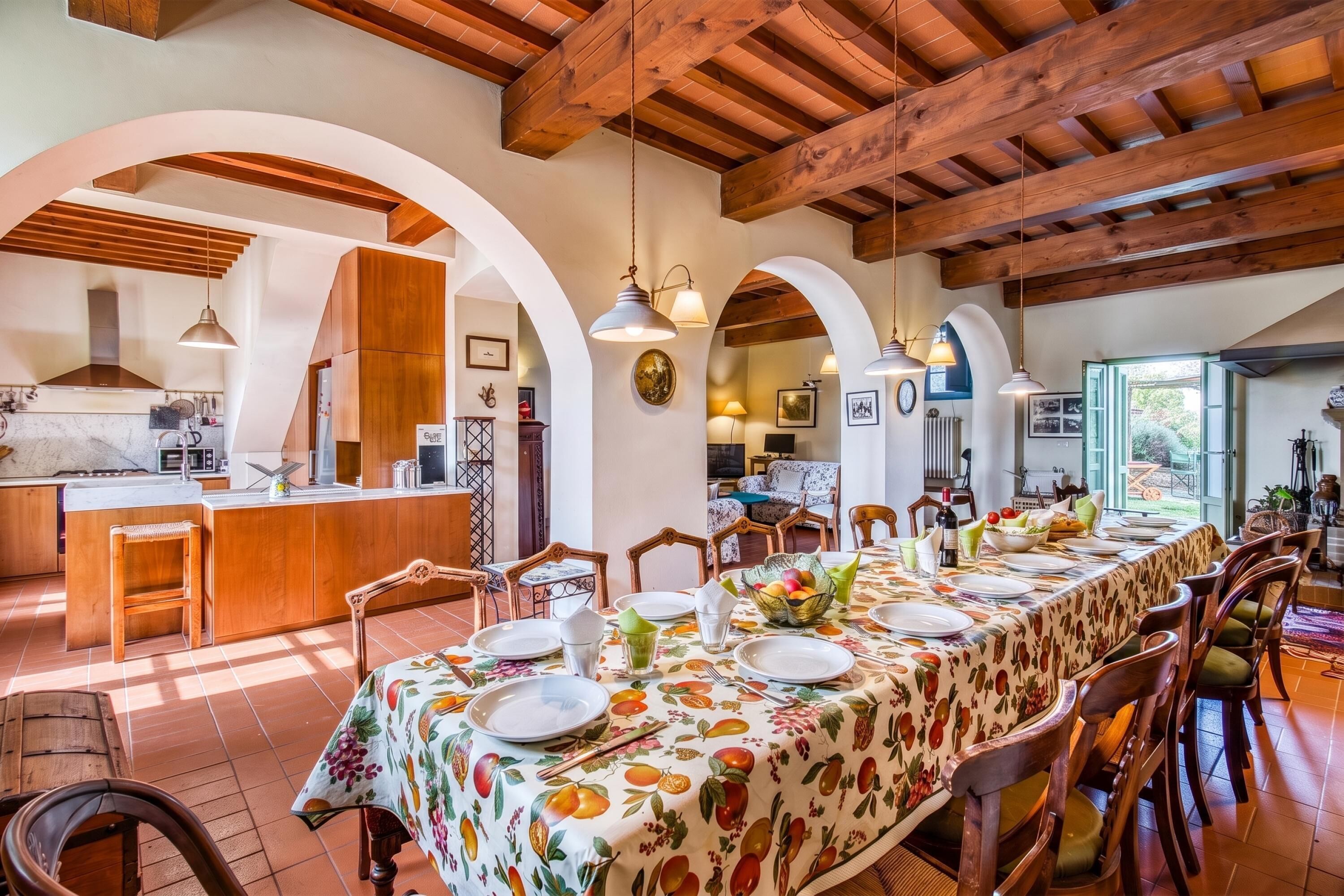 Uma sala de jantar espaçosa com uma mesa comprida posta para refeição, vigas de madeira no teto e uma cozinha ao fundo.