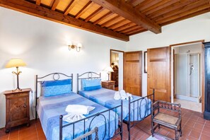 Una habitación con dos camas, techo de madera, una mesita con una lámpara y una puerta que da a un baño.