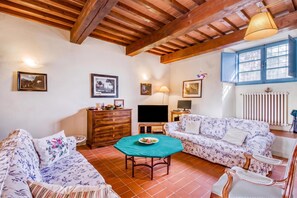Un salon chaleureux avec un plafond en bois, un ensemble de canapés, un téléviseur et une table à manger.