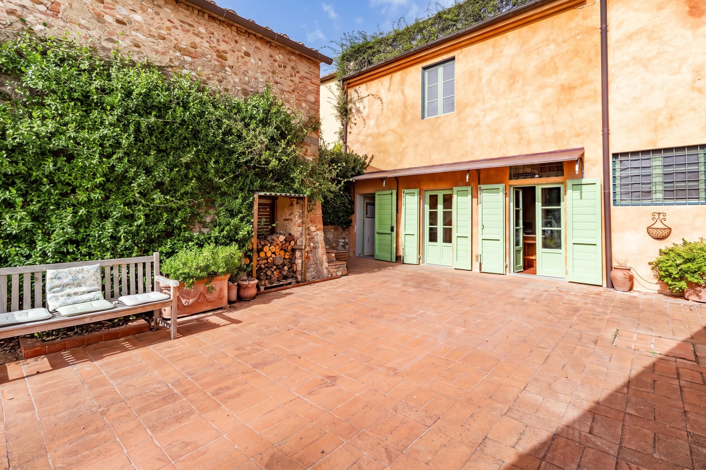 A courtyard with a bench, a stone wall, and a building with green shutters.