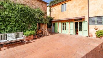 A courtyard with a bench, a stone wall, and a building with green shutters.