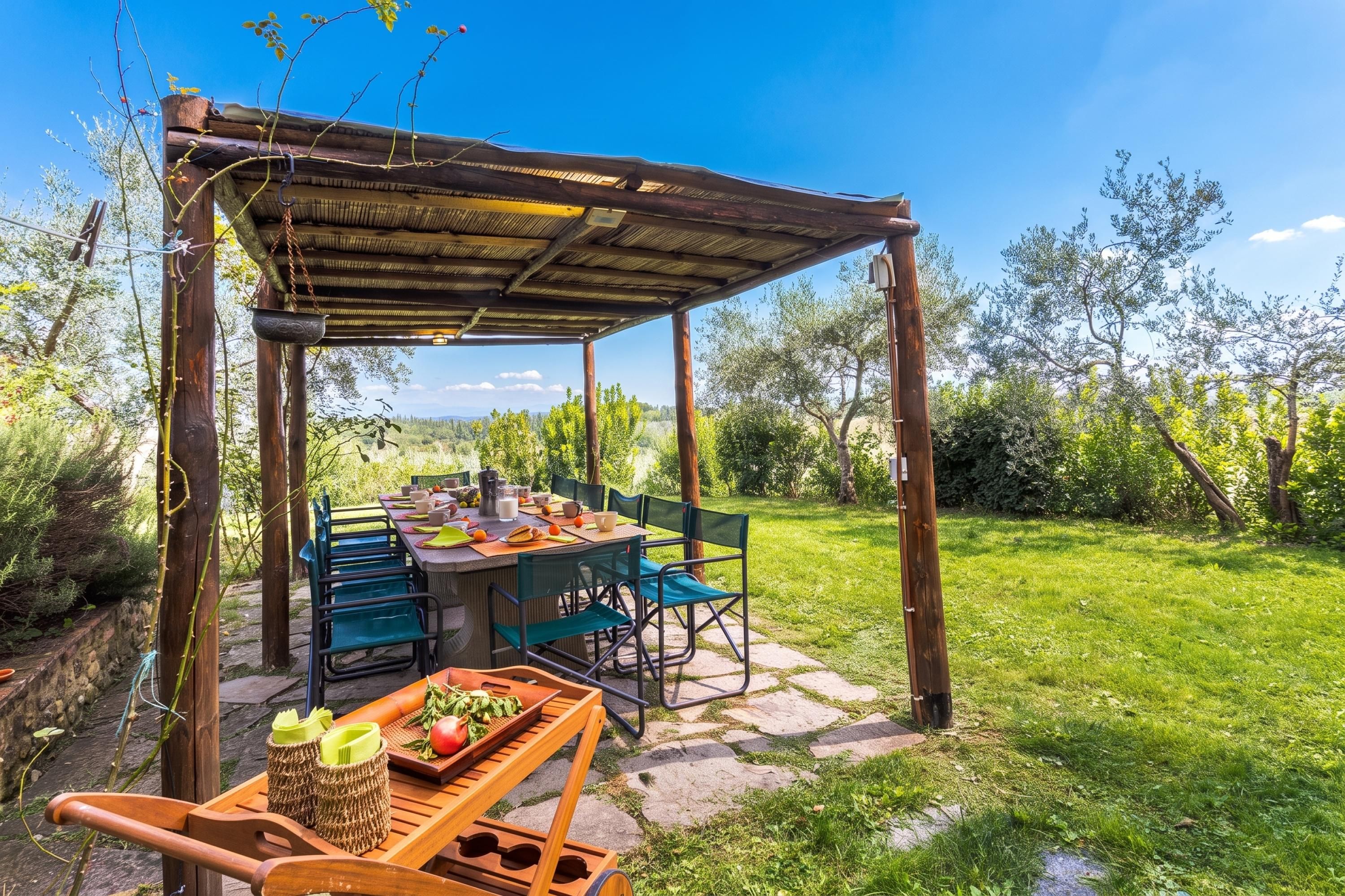 Un'area pranzo all'aperto con una pergola in legno rustico, pavimento in pietra e vista su un paesaggio verde e lussureggiante.