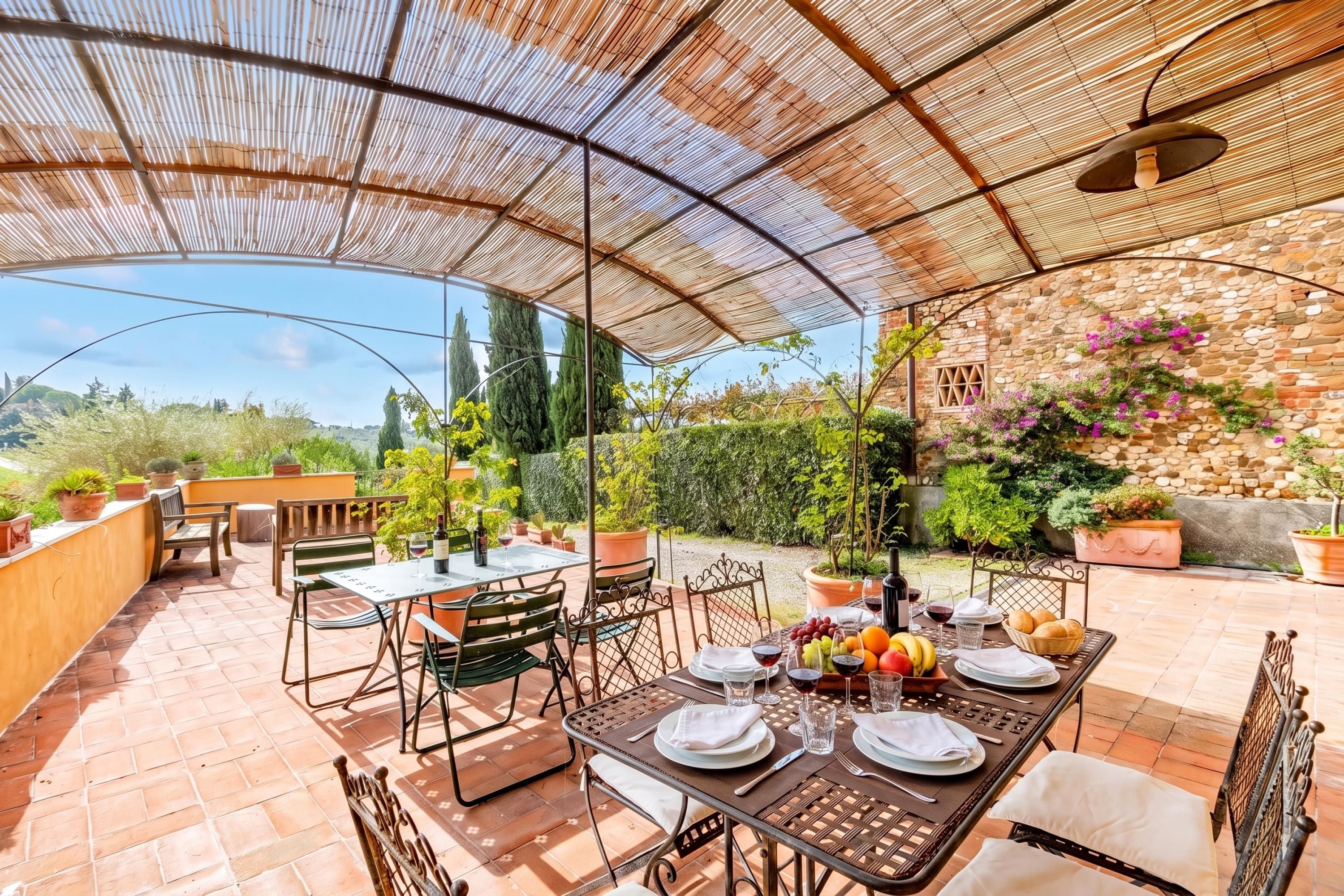 Une terrasse extérieure dotée d’un espace repas couvert, de tables, de chaises et de plantes en pot.