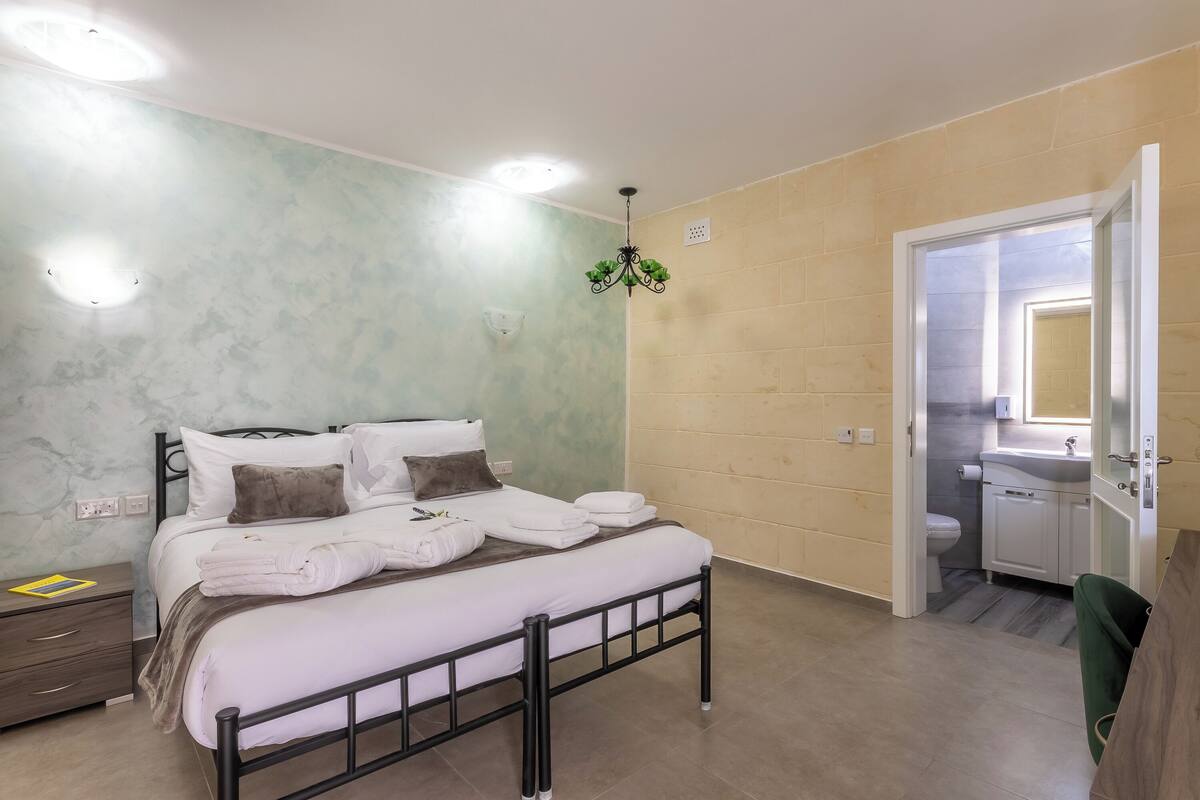 A bedroom with a bed, bedside table, and a bathroom visible through an open door.