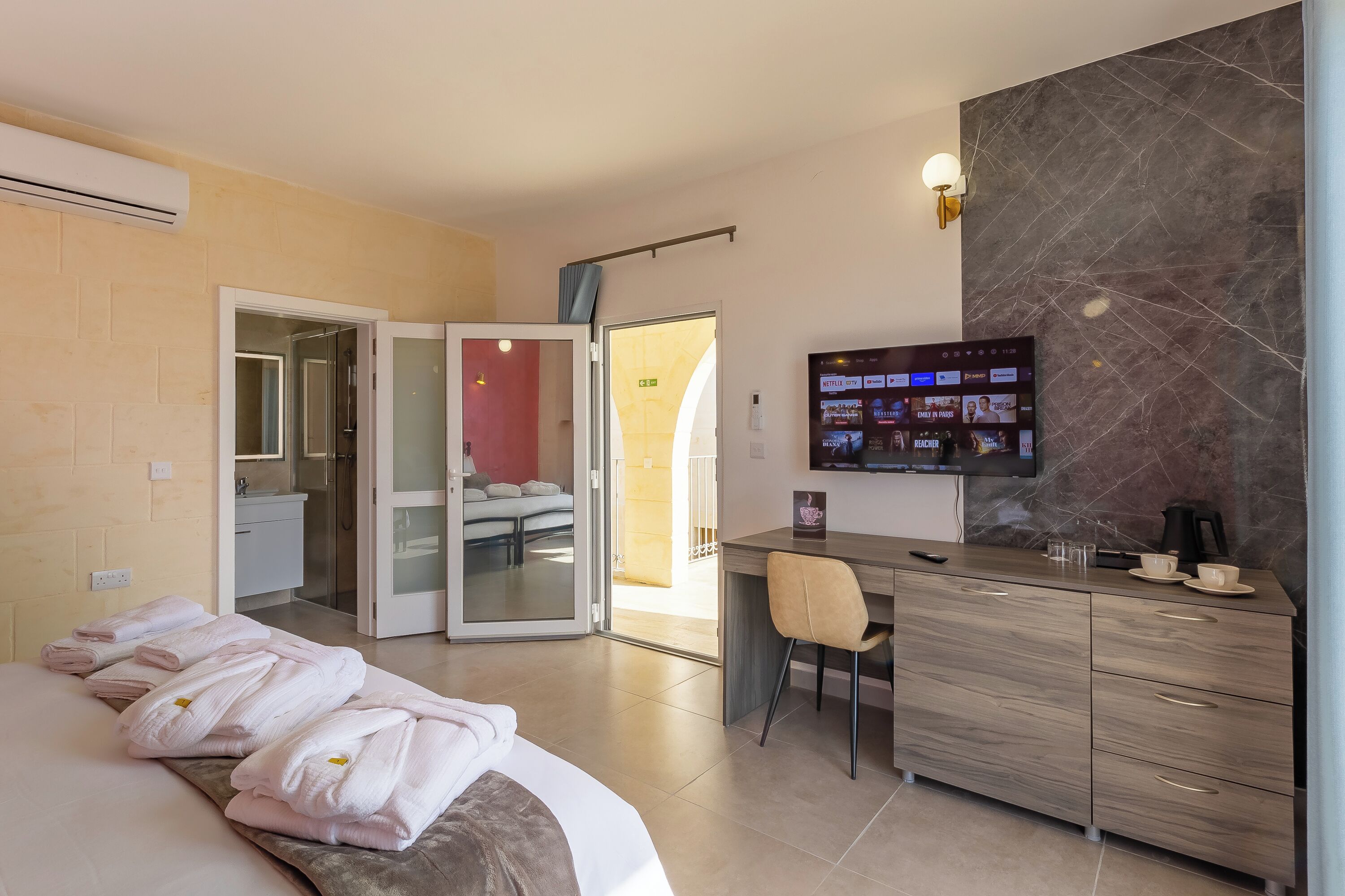 A hotel room with a bed, a desk with a chair, a TV, and a bathroom with a shower and toilet.