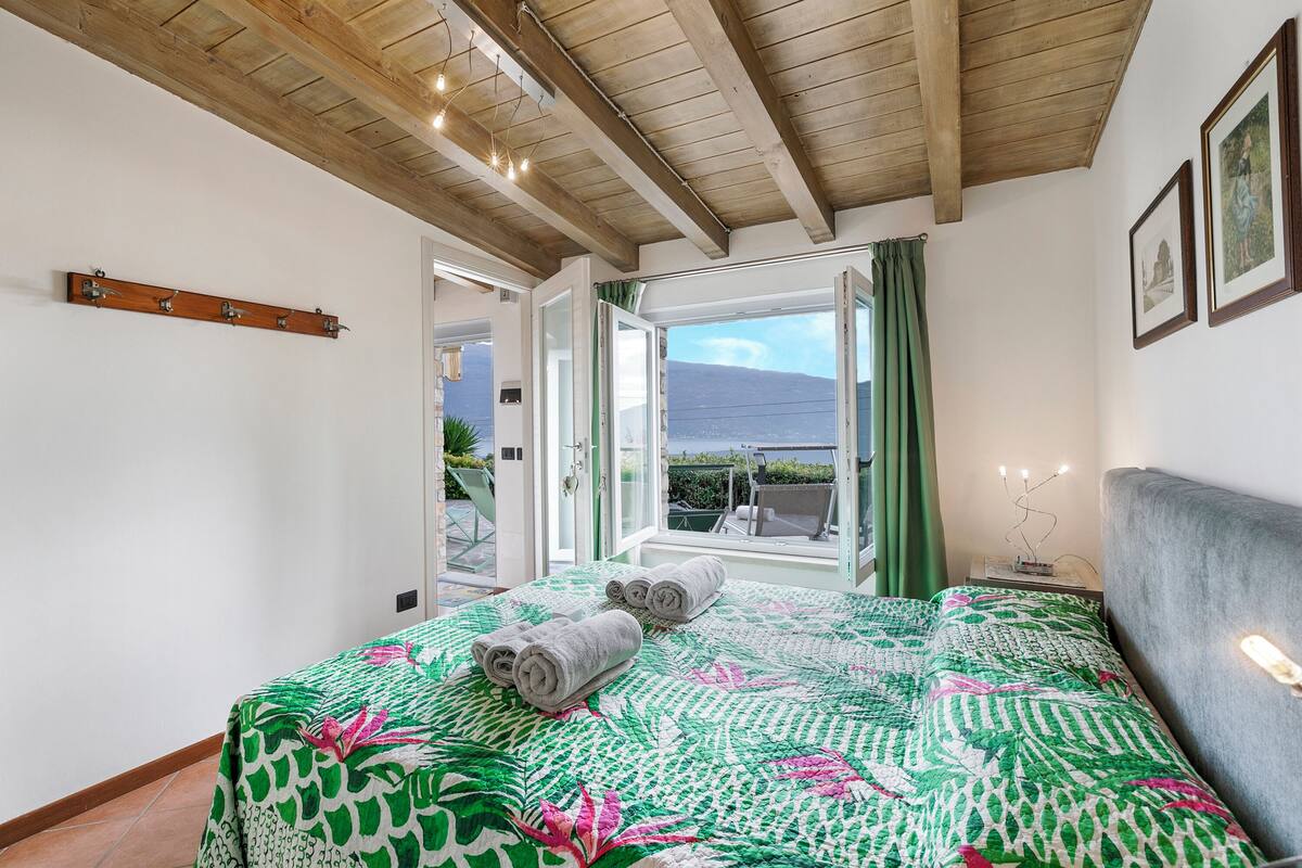 A bedroom with a large bed, a wooden ceiling, and a view of the outdoors.