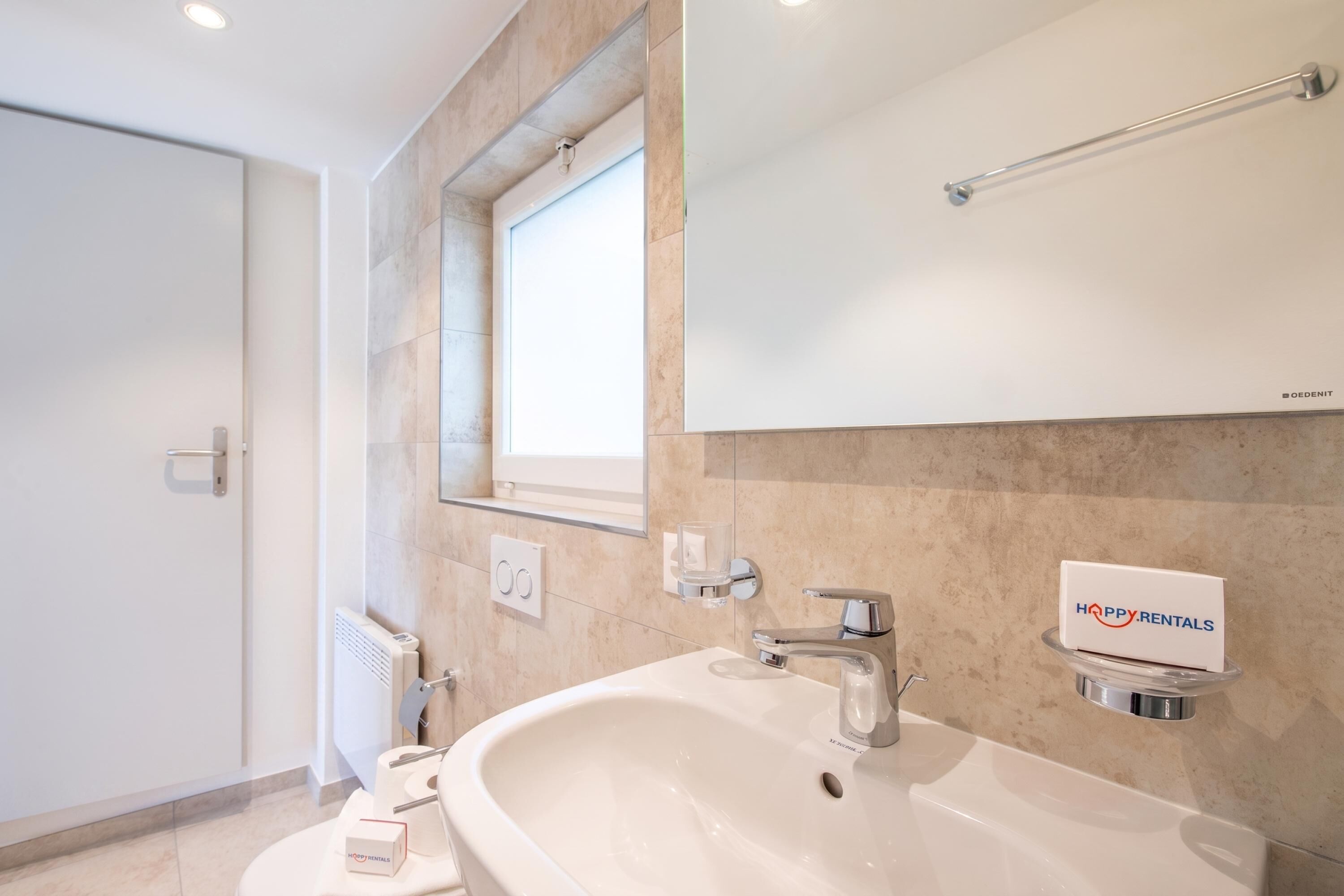 Un baño moderno con lavamanos blanco, grifo cromado y toallero.
