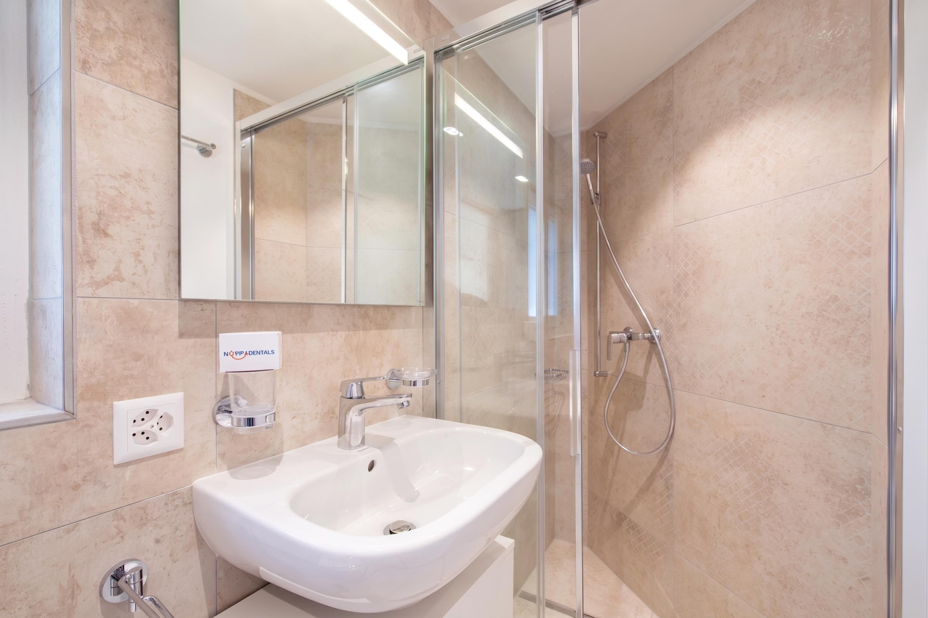 Un baño moderno con un lavamanos blanco, una cabina de ducha de vidrio y un espejo sobre el lavamanos.